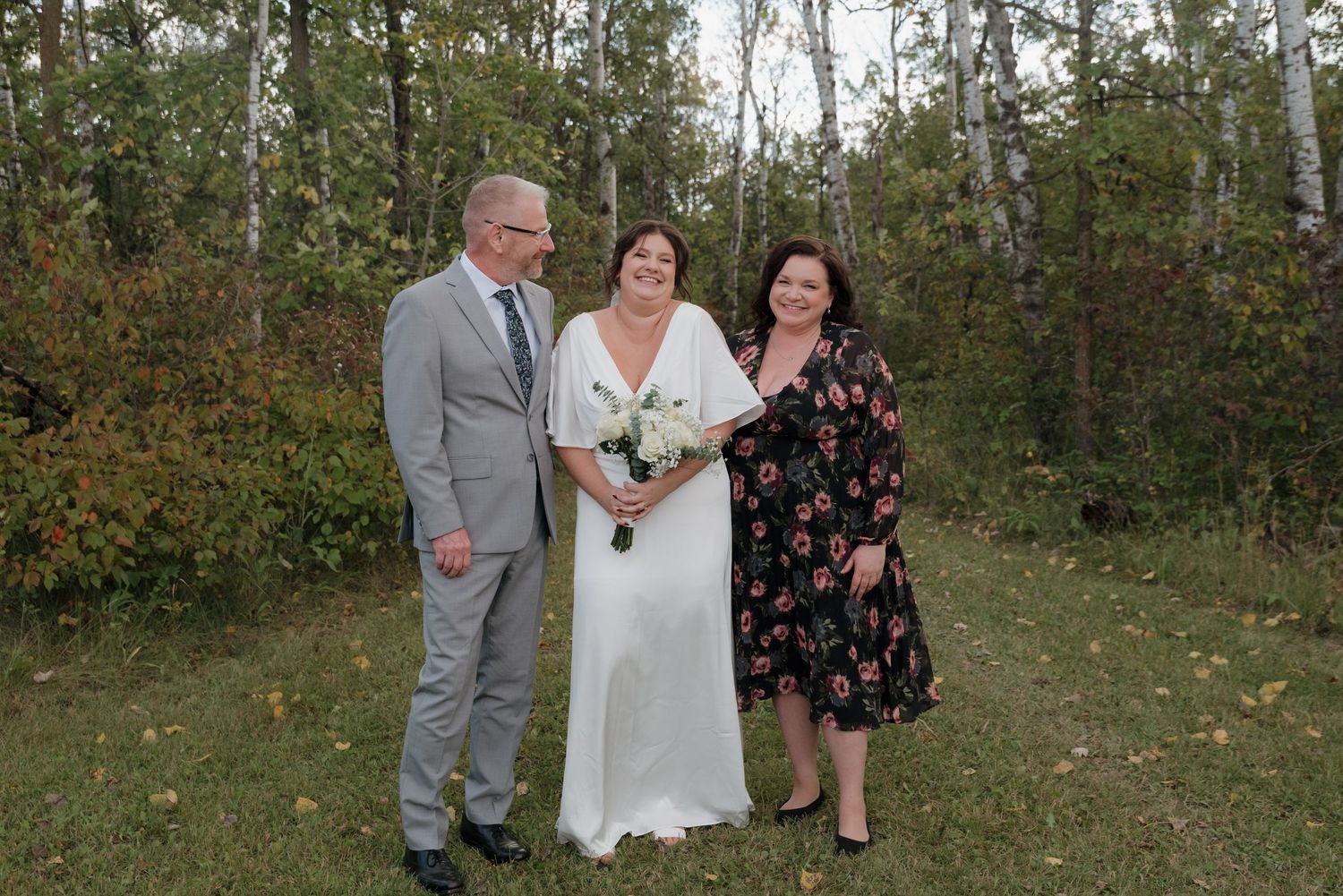 A wedding party poses for a portrait in a wooded setting with fall foliage.
