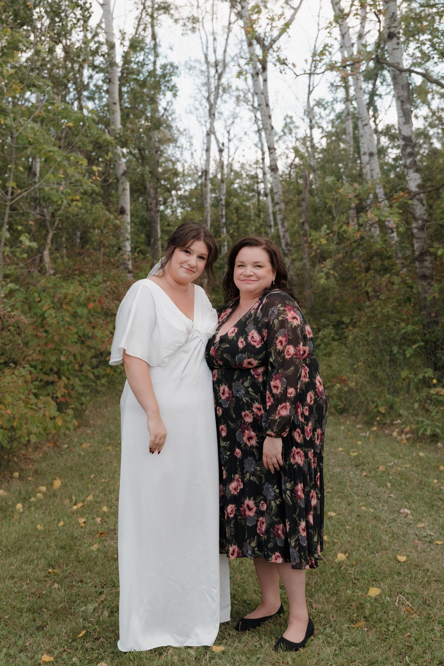 A serene outdoor portrait shows two lovely friends in formal dresses against a wooded backdrop in autumn.