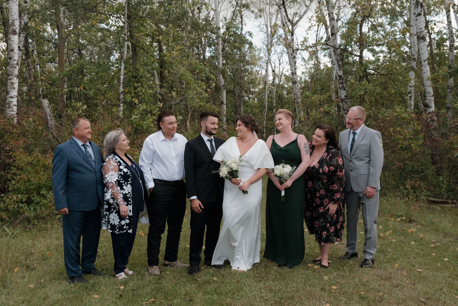 A bridal party poses together for a formal portrait outdoors in a wooded setting.