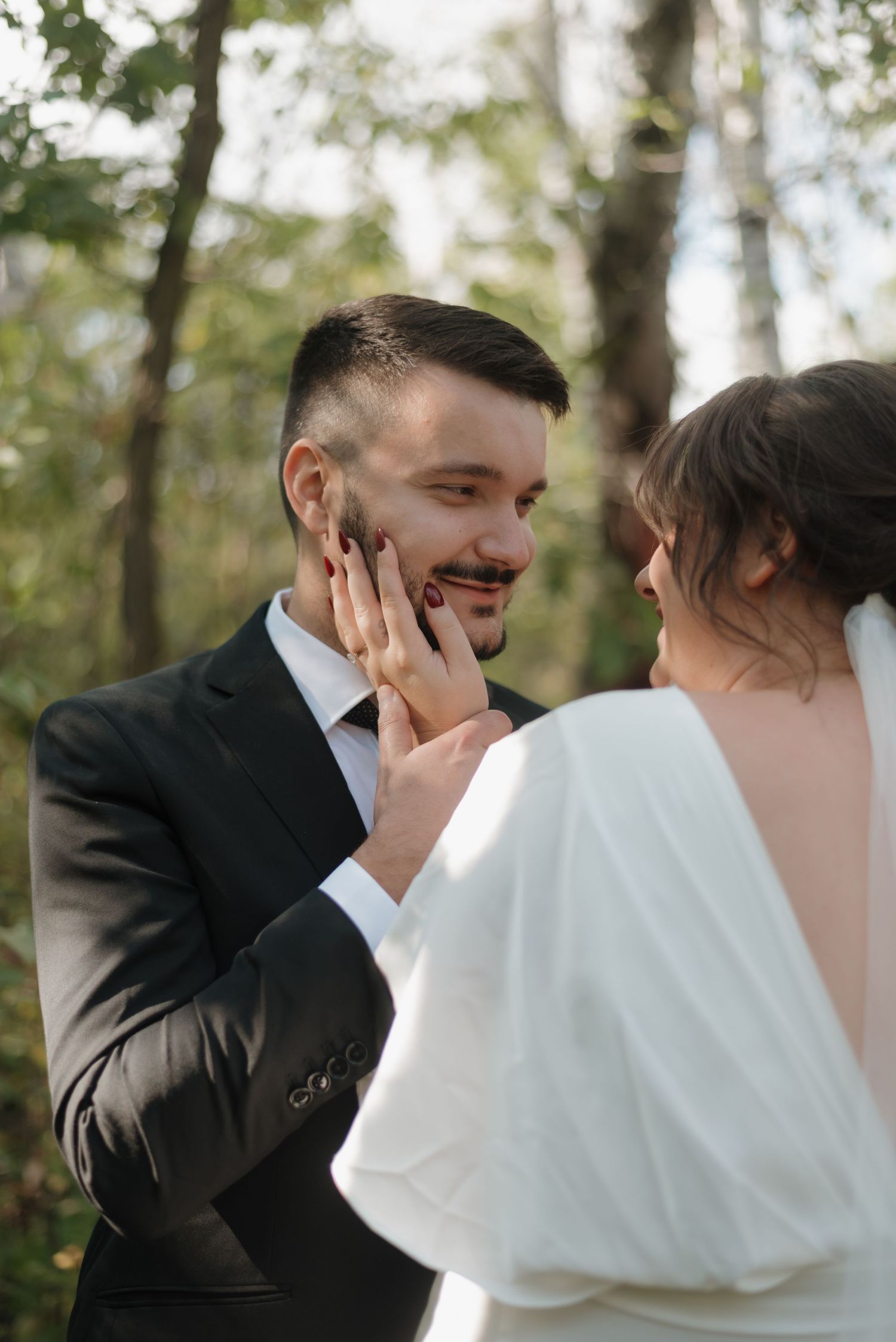 A tender wedding moment between newlyweds in formal attire captured in the forest during their romantic photoshoot.