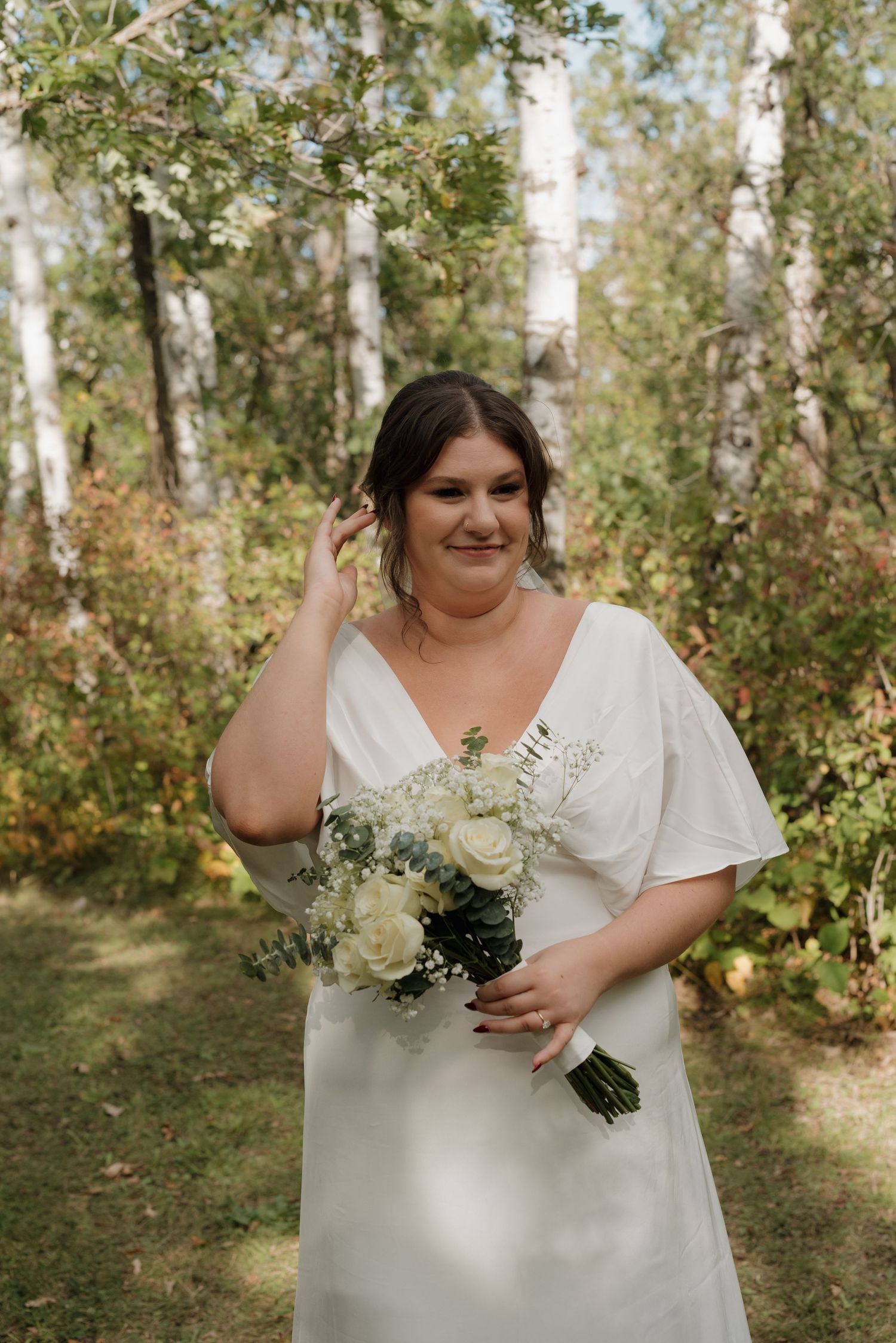 White bouquet of flowers held against a backdrop of birch trees and greenery in a natural woodland setting.