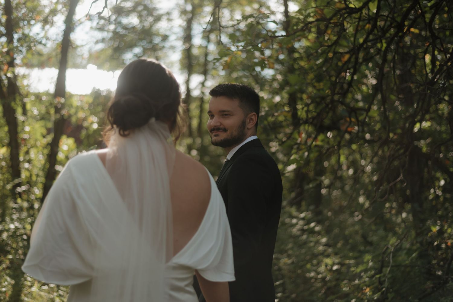 A couple shares an intimate moment during their wedding ceremony in a sunlit forest setting.