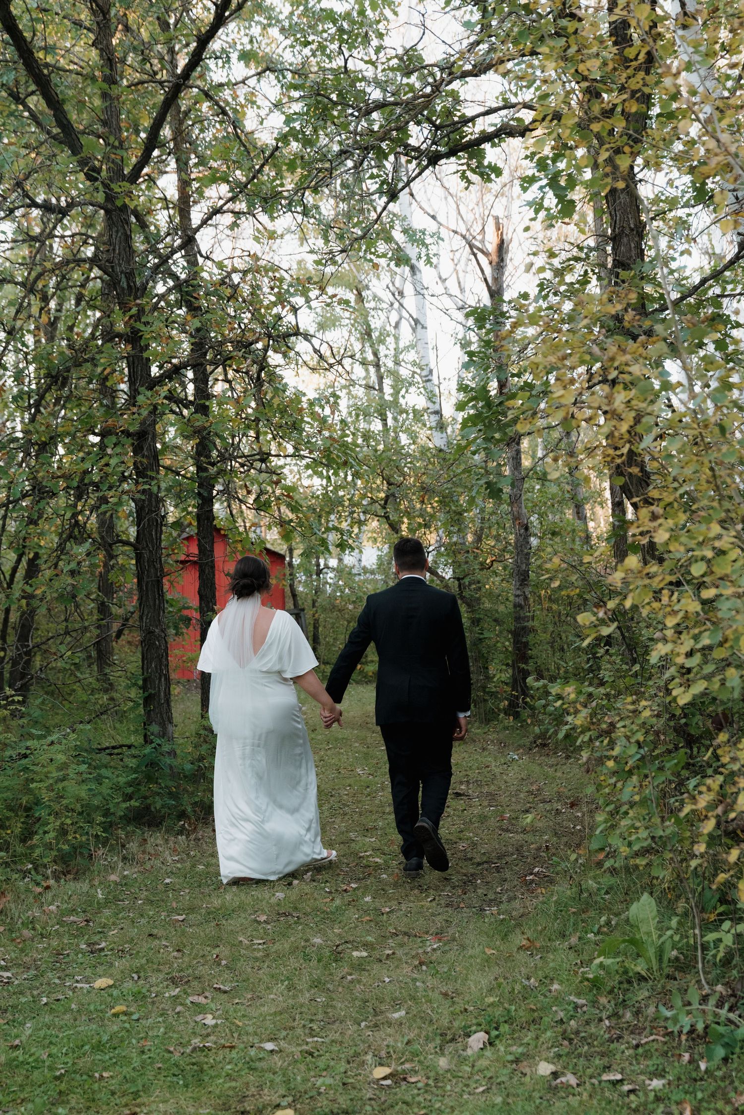 Newlyweds holding hands while walking down a wooded trail during their autumn wedding.