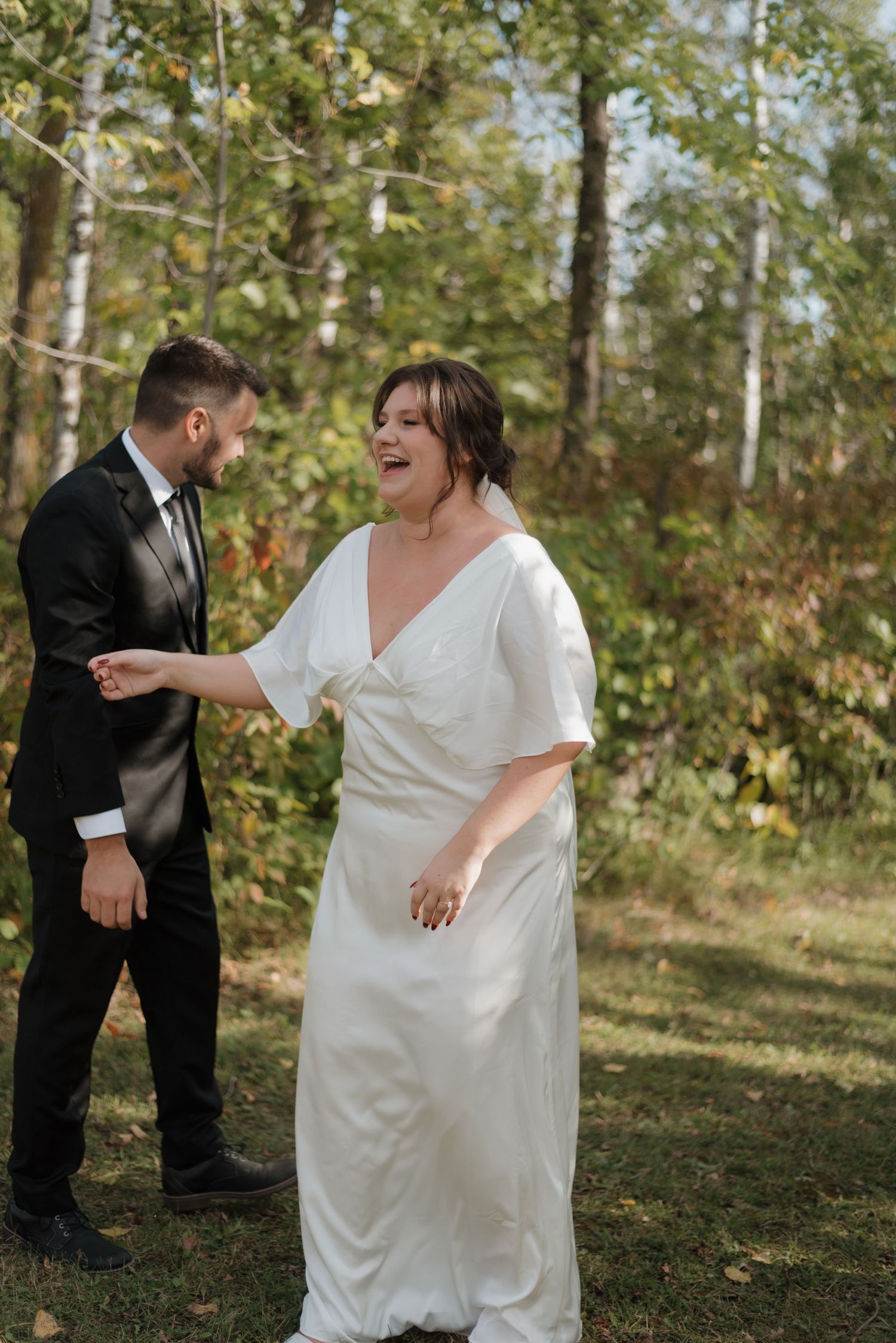 Playful newlyweds share a joyful moment in a wooded outdoor setting during their wedding photoshoot.