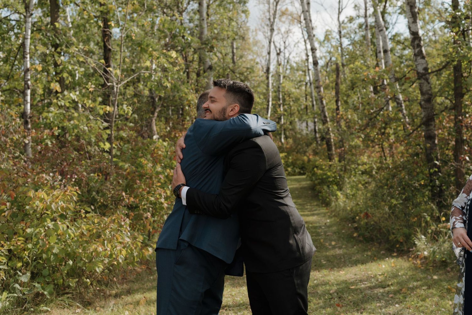 Two people share an emotional embrace on a forest trail during a wedding ceremony.