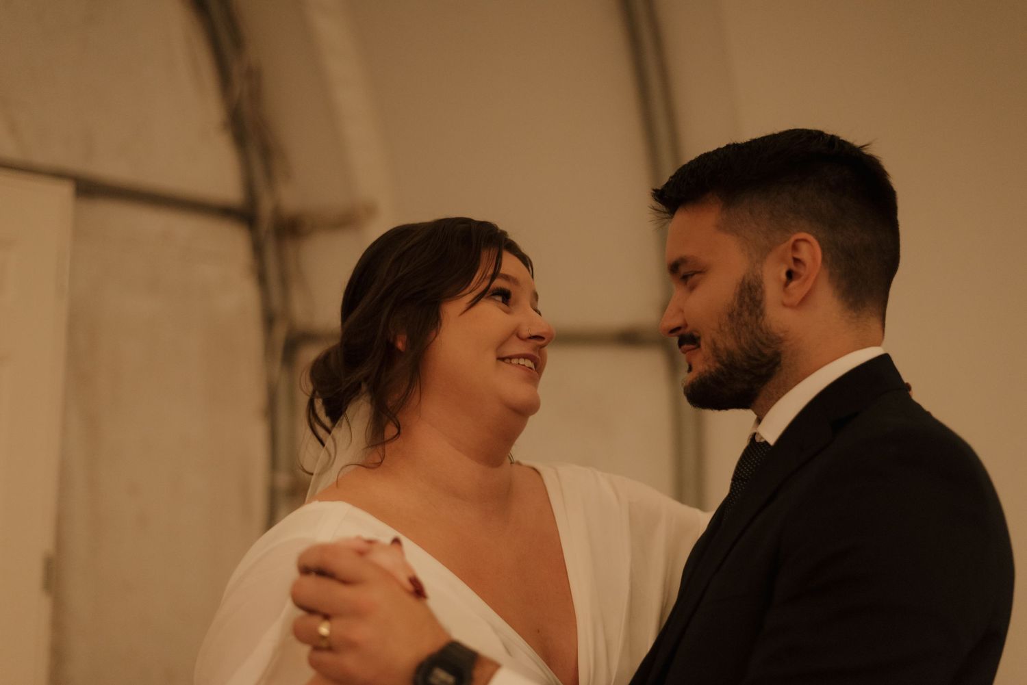 A couple shares an intimate moment together during their first dance at their wedding reception in warm lighting.