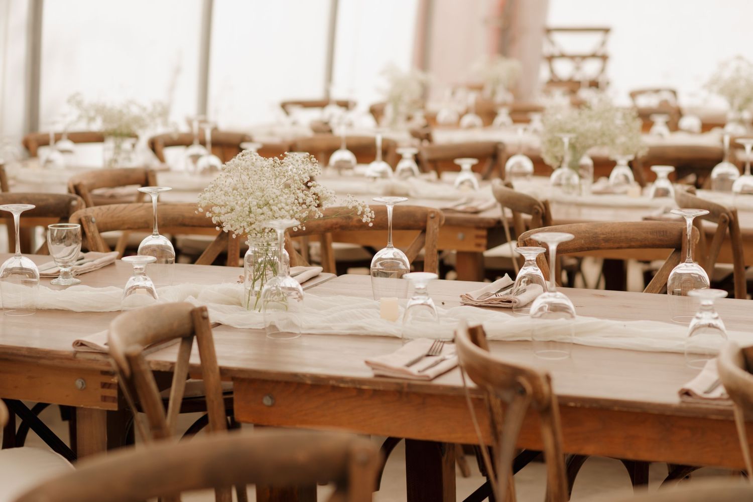 Rustic wooden tables set for a wedding reception with delicate white floral centerpieces and elegant place settings.