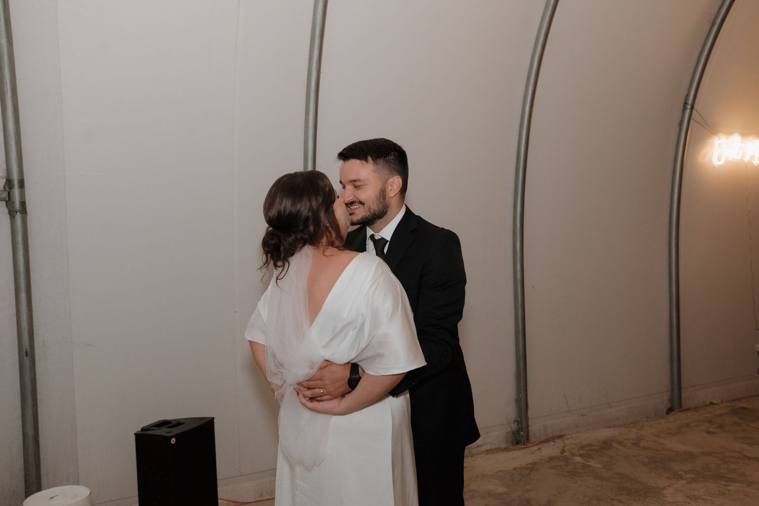 Couple shares an intimate moment during their first dance in minimalist wedding venue with curved white walls.