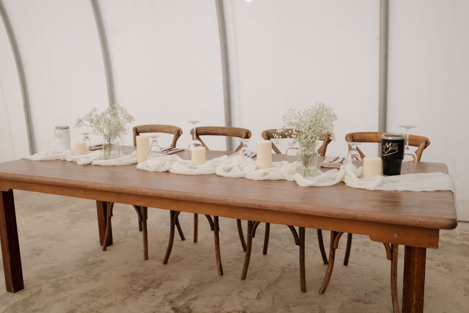 Long wooden banquet table with simple white place settings and wooden chairs in a minimalist style.
