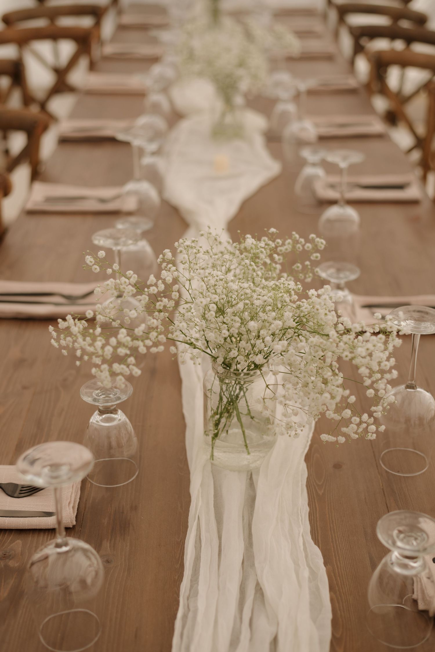 Long wooden table adorned with white runner and baby's breath centerpieces for wedding reception.