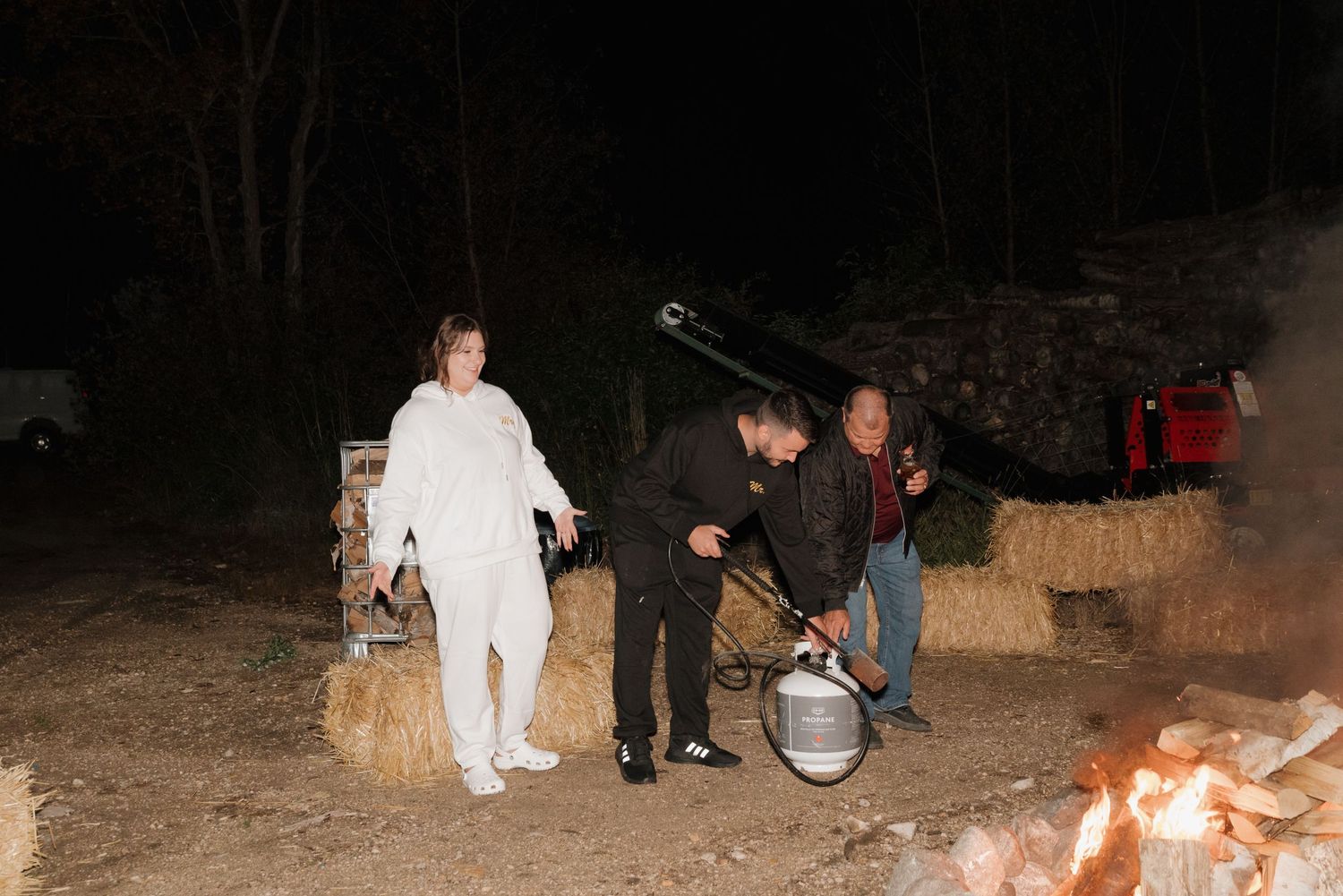 Nighttime wedding celebration with guests gathered around hay bales and musical instruments.