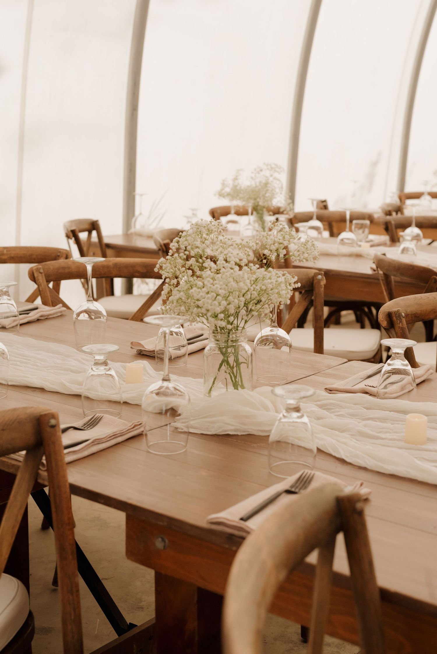 Rustic wedding reception setup with wooden chairs and delicate floral centerpieces in tent venue.