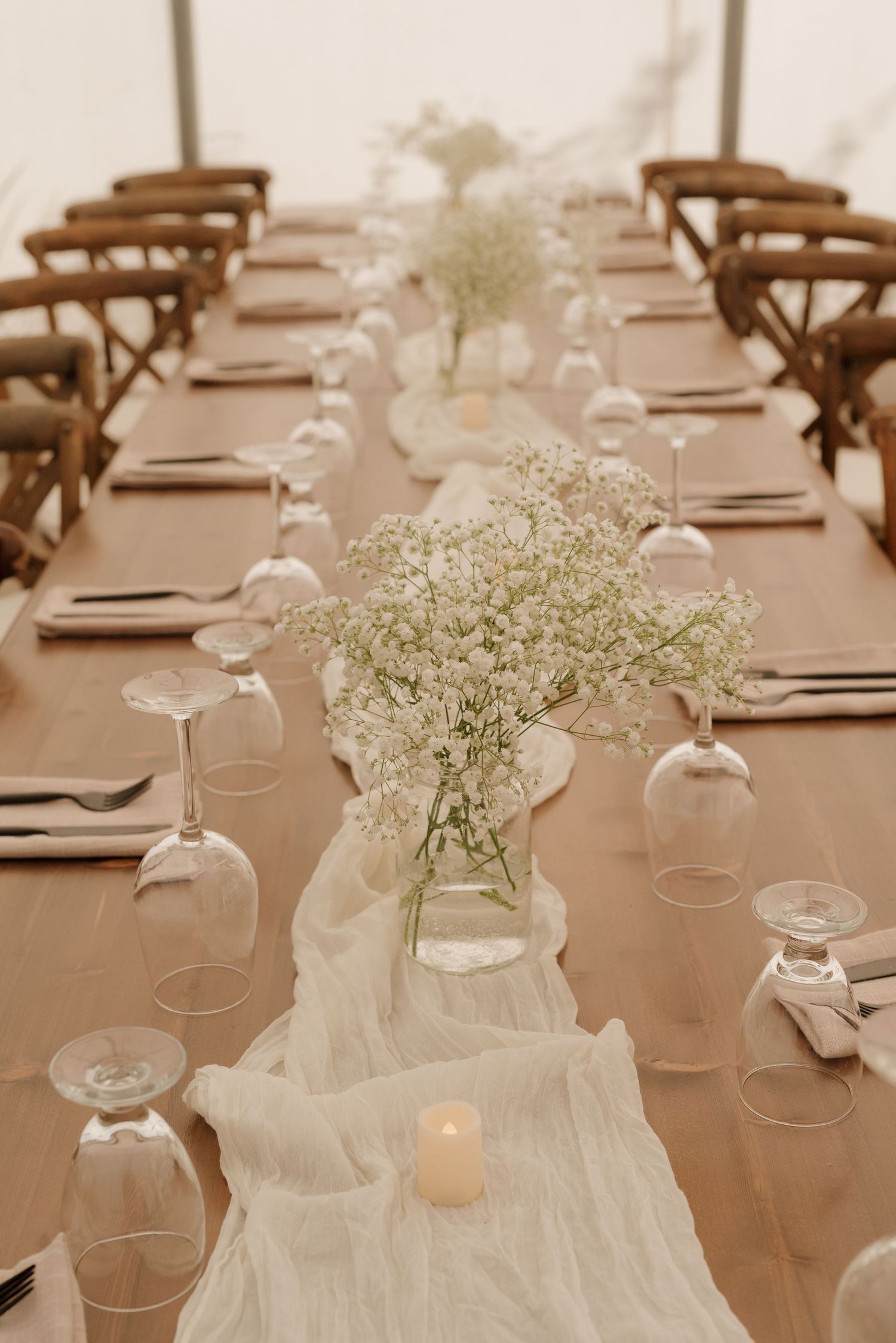 Wedding table decor featuring white runner, baby's breath arrangements and tealight candles.