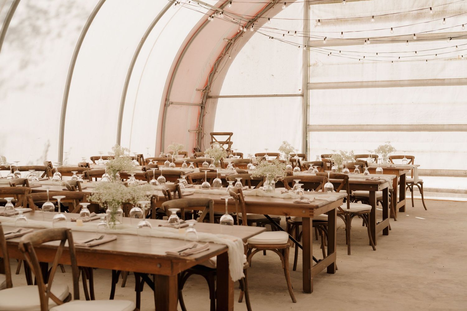 Vintage sepia photograph of an empty event space with rows of decorated dining tables under an arched tent structure.