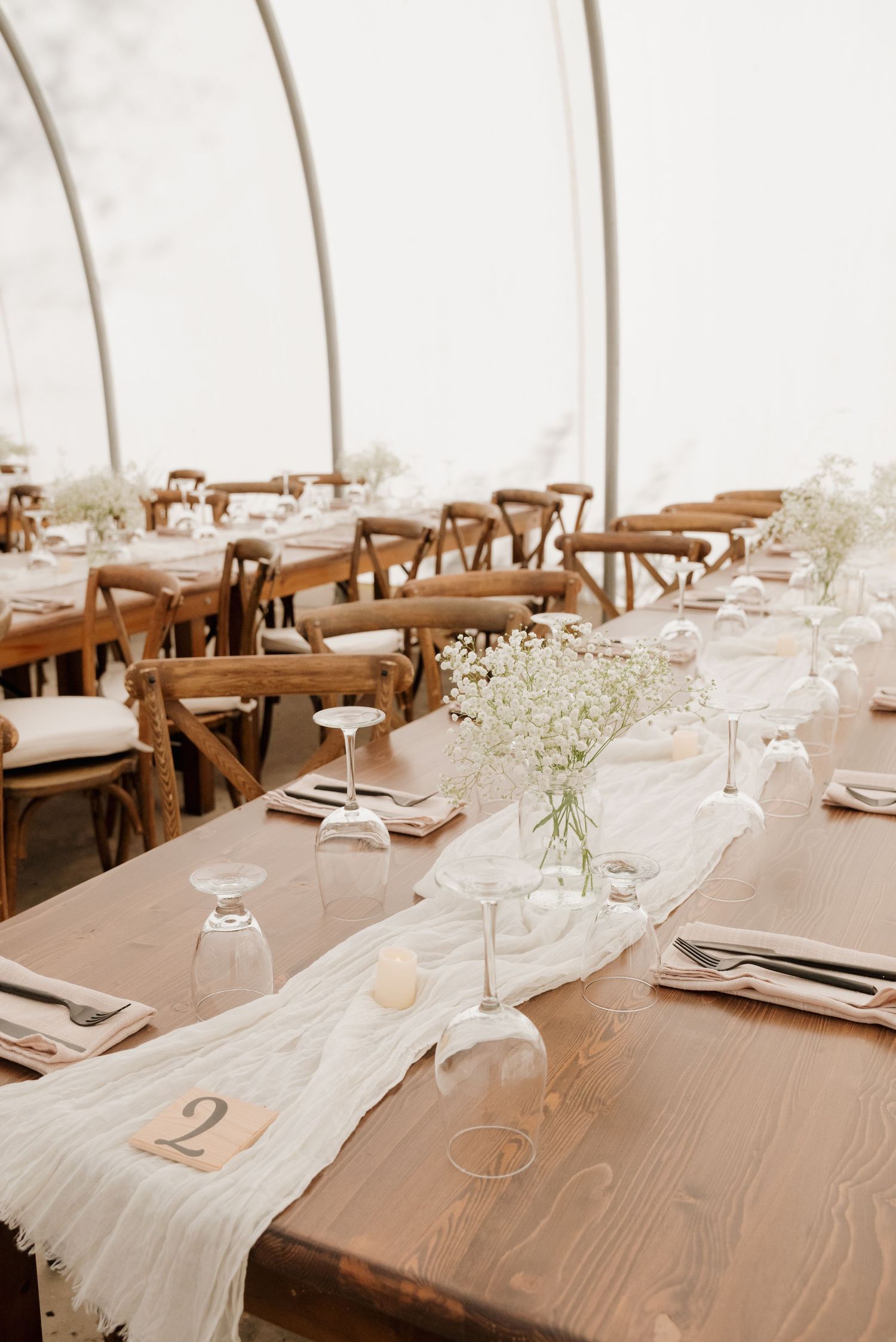 Long wooden farm tables set for wedding reception with white runners and delicate baby's breath centerpieces.