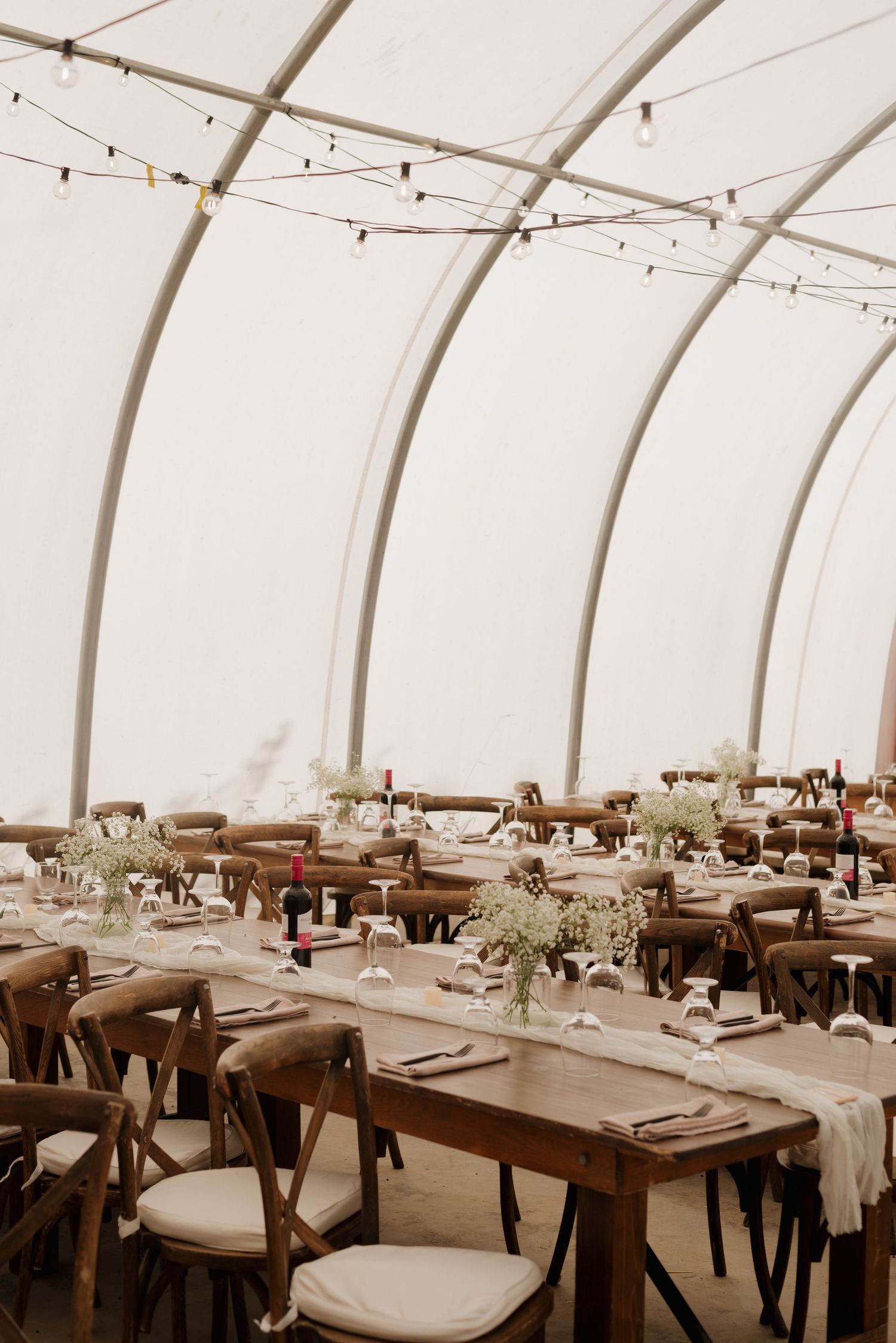 Elegant tent venue with string lights and rustic wooden tables set for wedding reception.