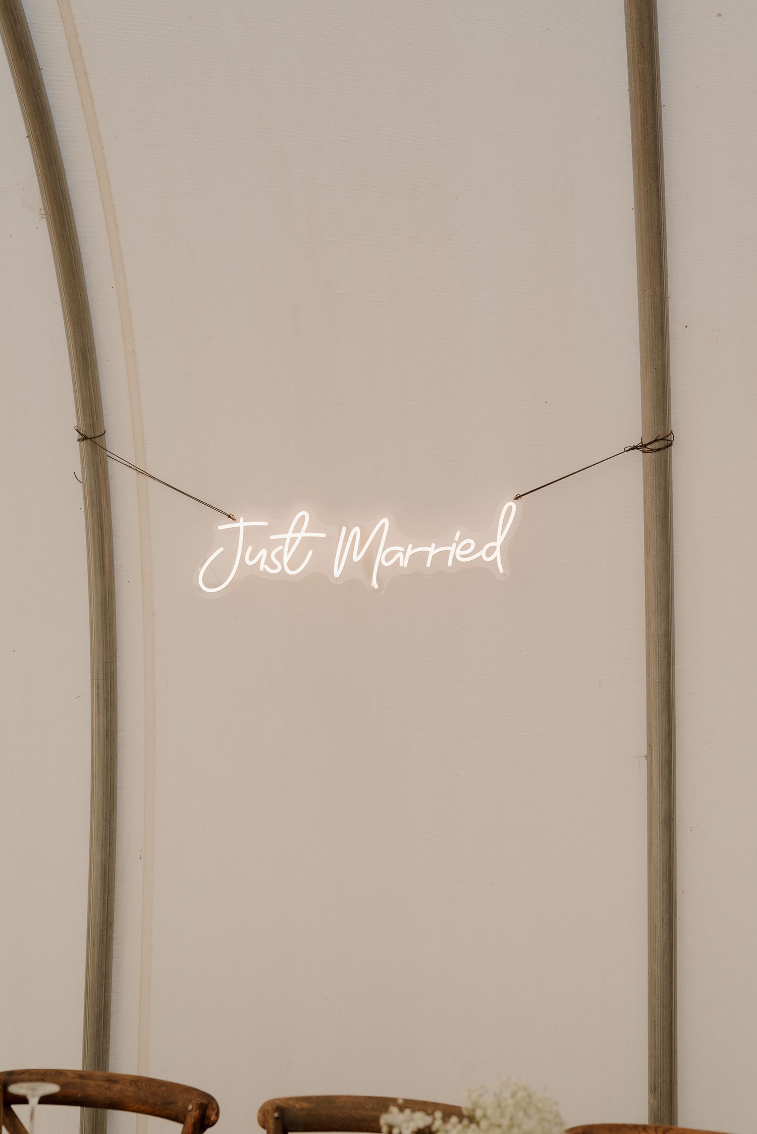 A glowing white neon 'Just Married' sign hangs against a beige wall at a wedding reception venue.
