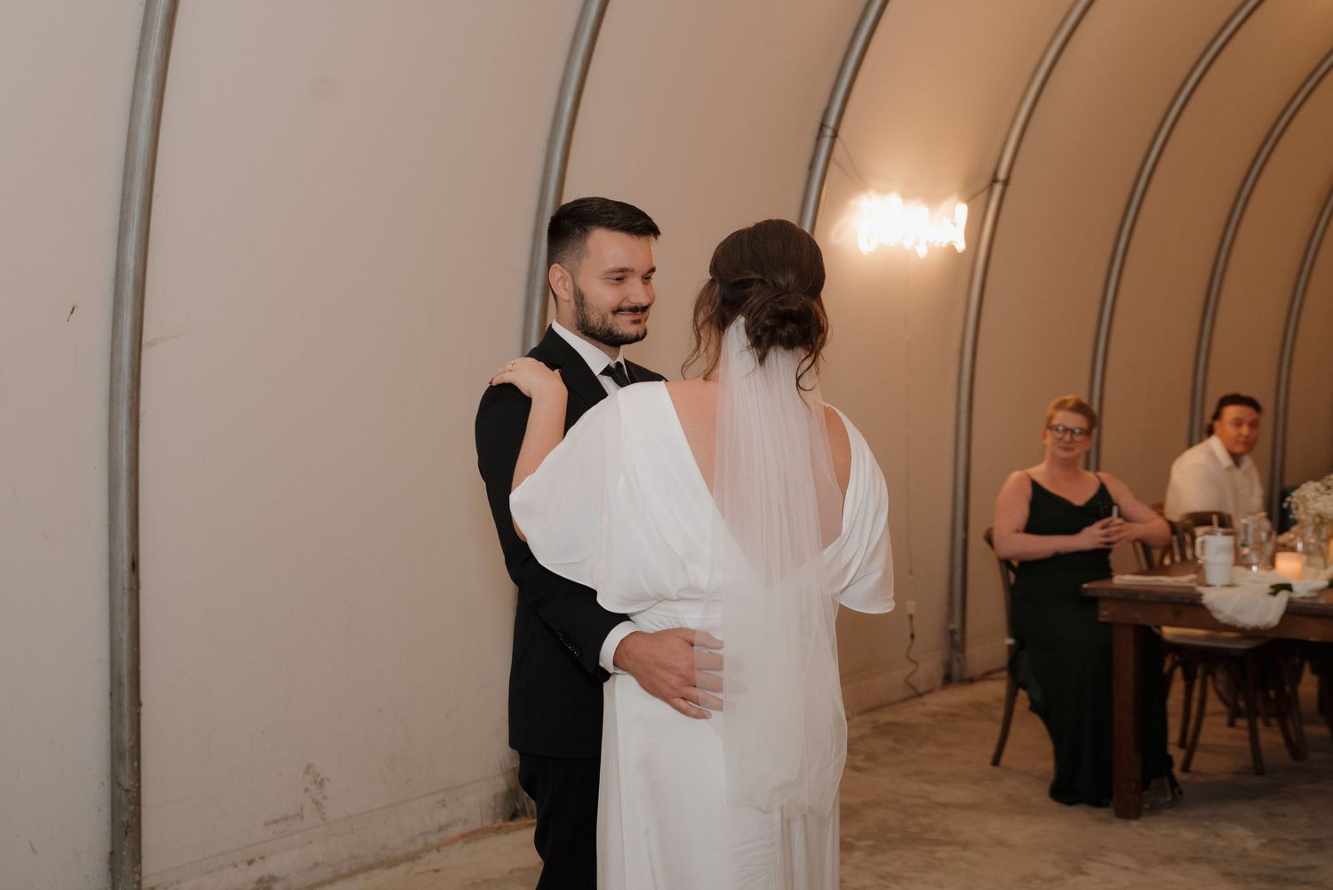 A couple shares their first dance at a wedding reception in an arched industrial-style venue.