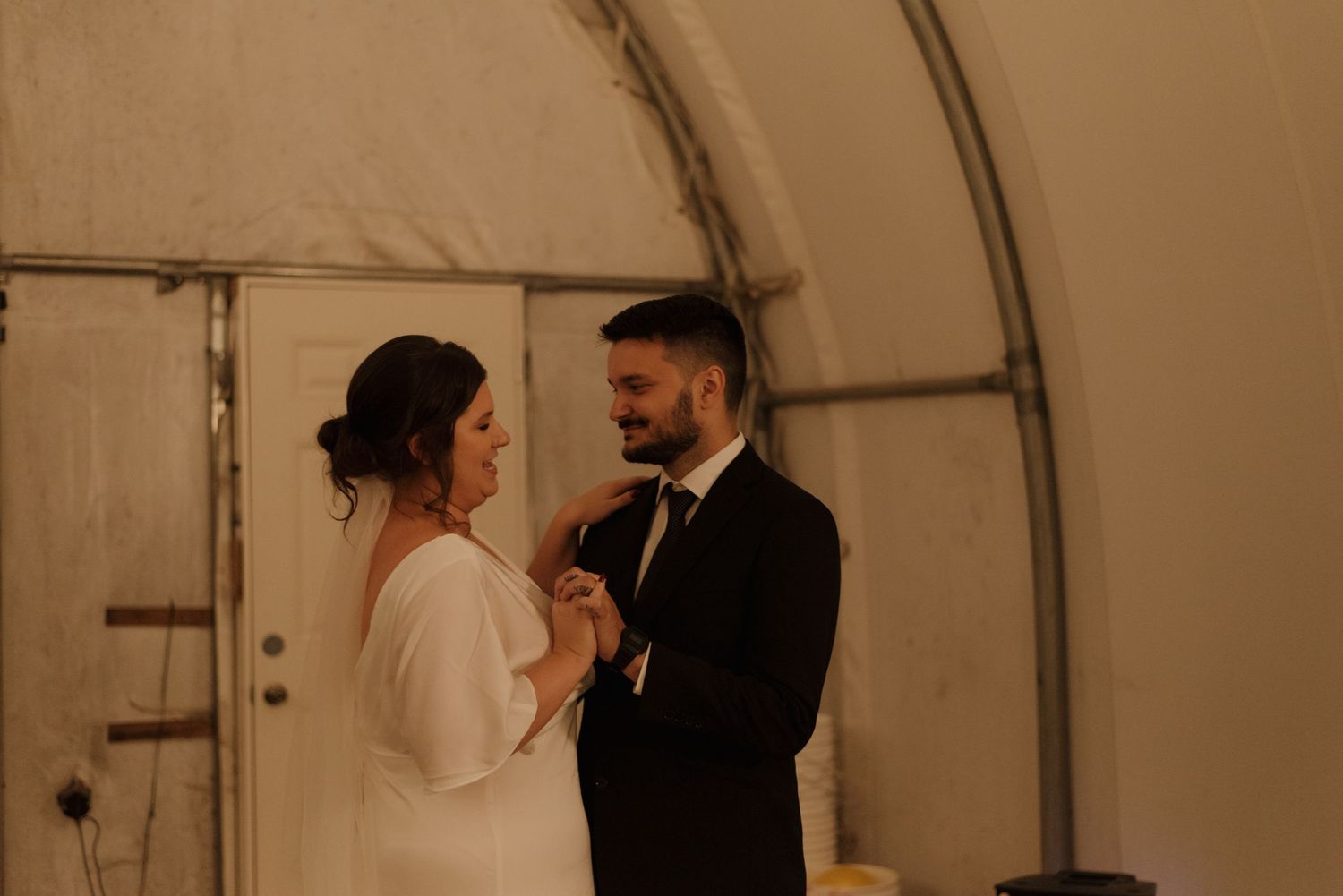 A couple sharing an intimate moment in a white tent structure with warm lighting.
