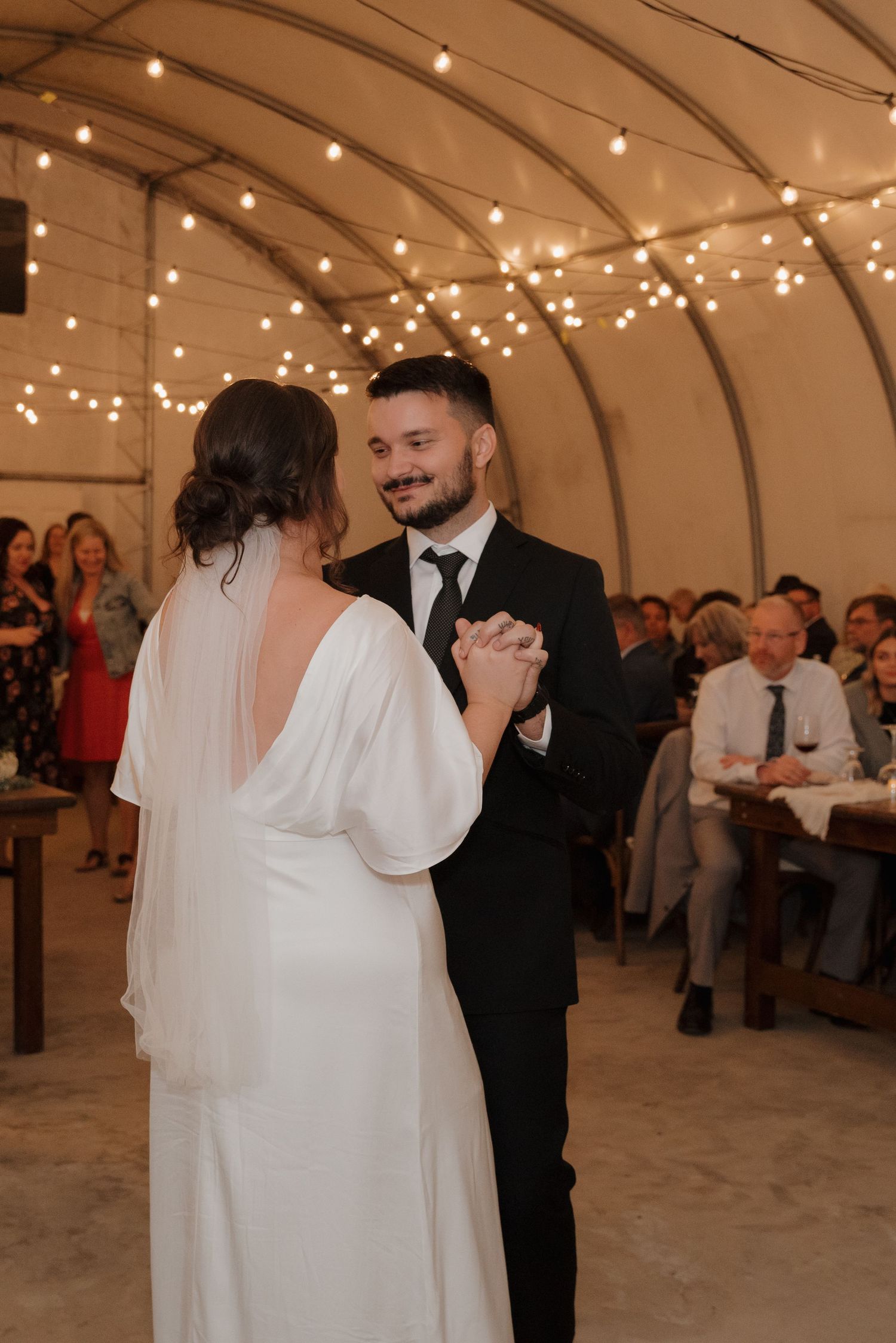 Romantic first dance under twinkling string lights in a reception venue.