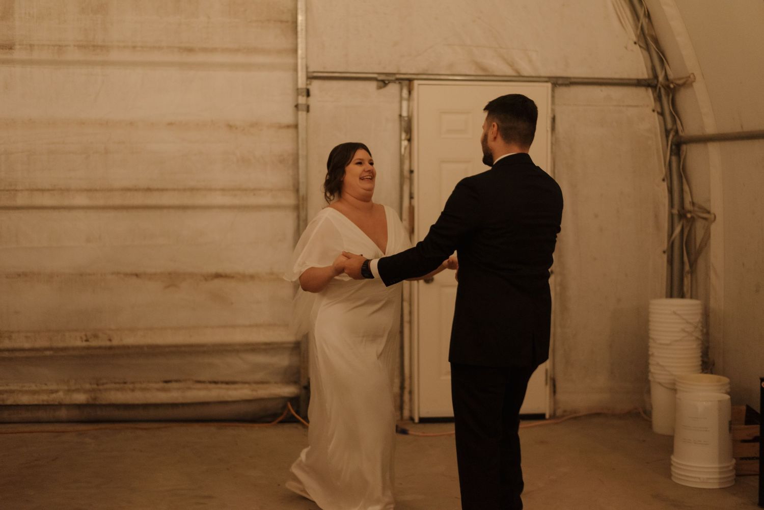 Wedding couple dancing in an intimate moment inside a simple white tent venue.