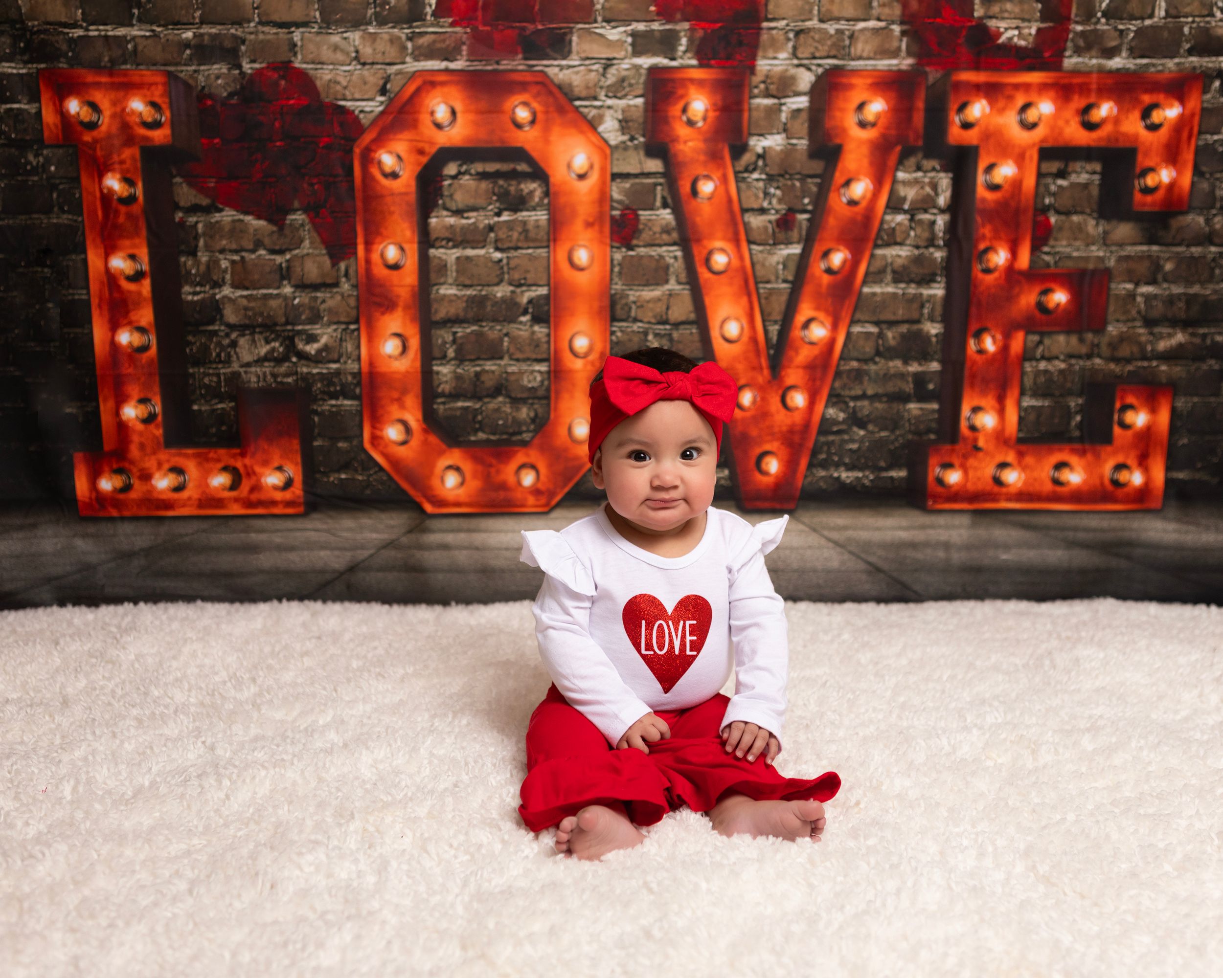 Red illuminated LOVE letters create romantic backdrop against textured brick wall.