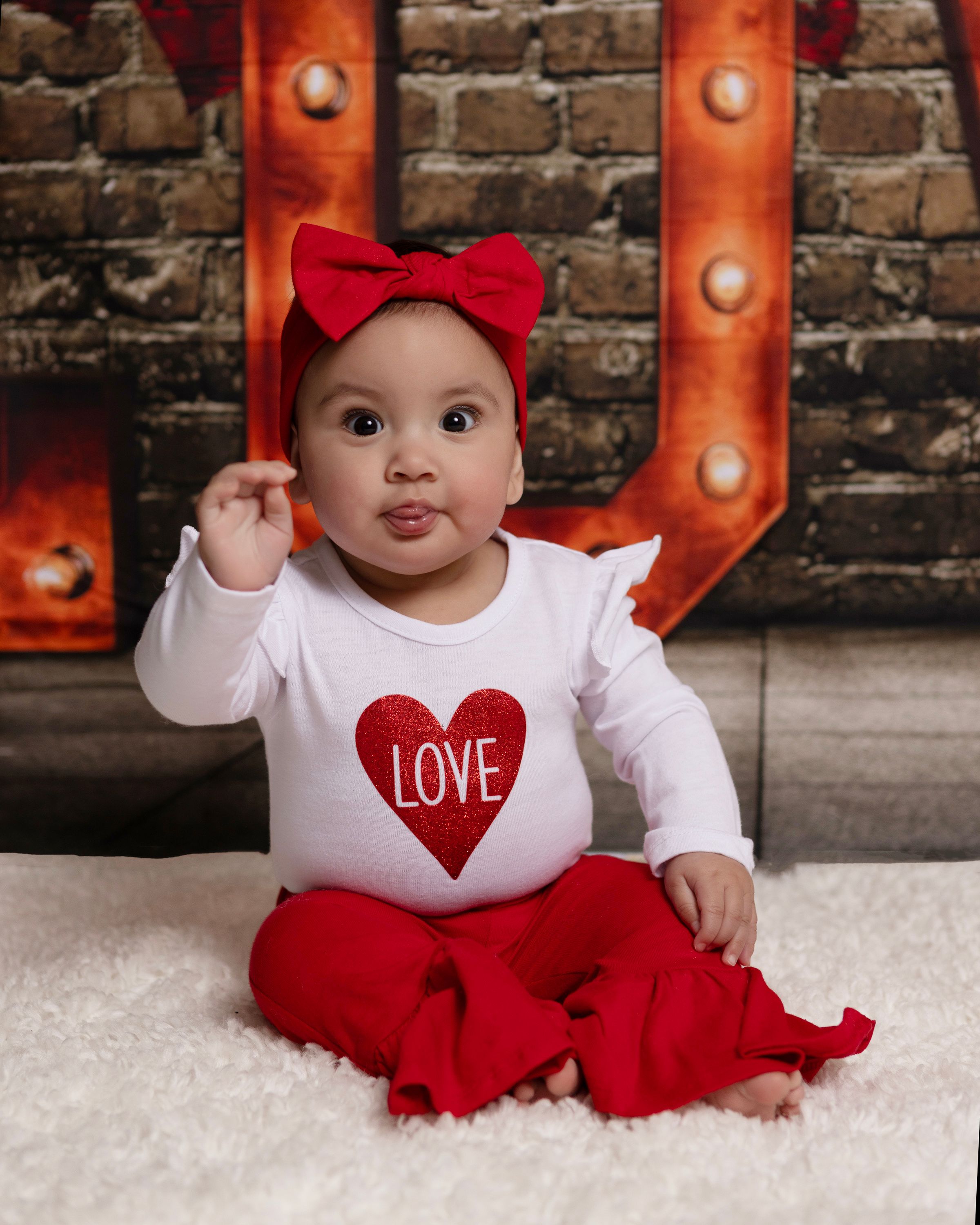 Valentine's themed photo setup with red LOVE marquee sign against brick background.
