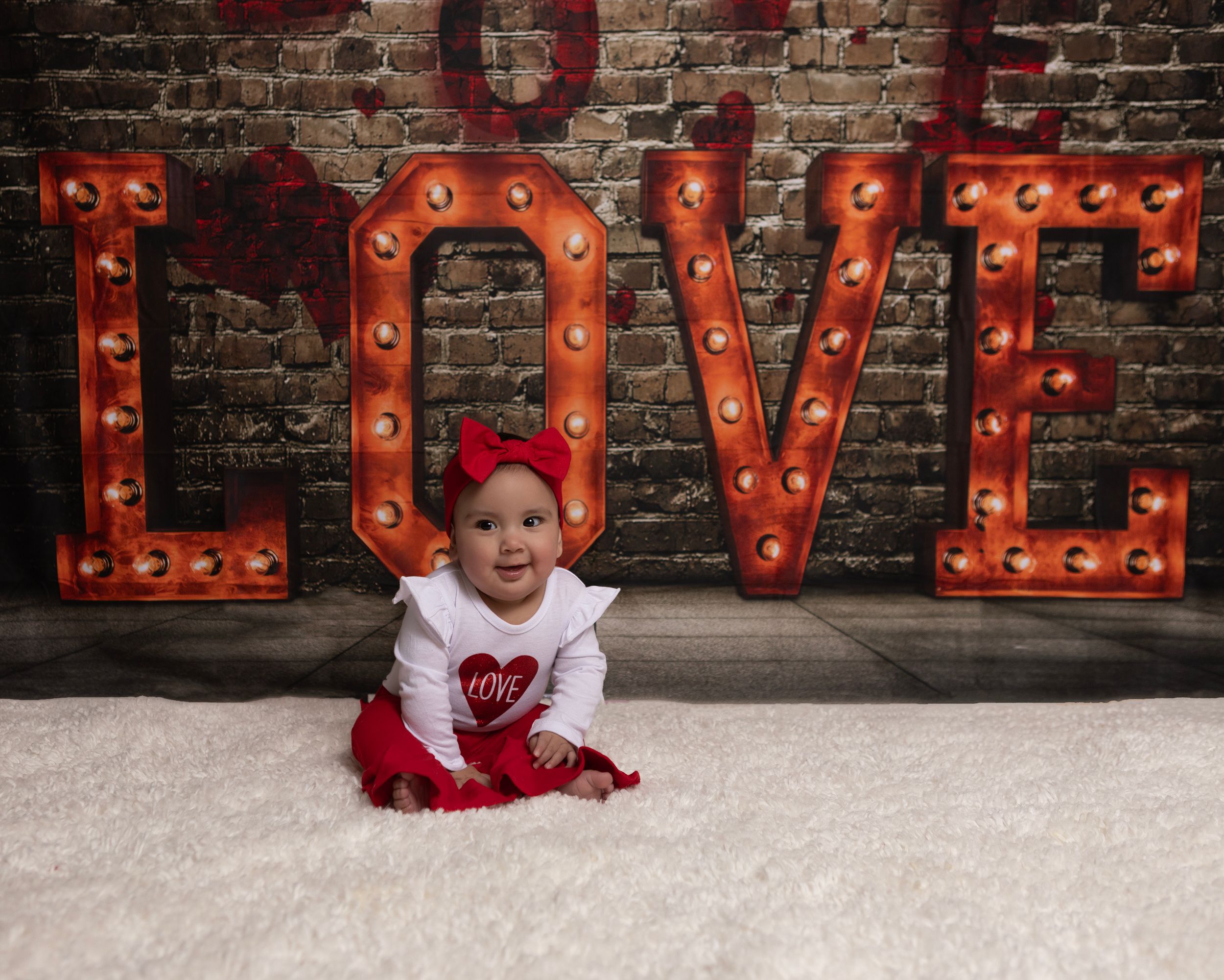 Red marquee LOVE letters illuminate against rustic brick wall backdrop.