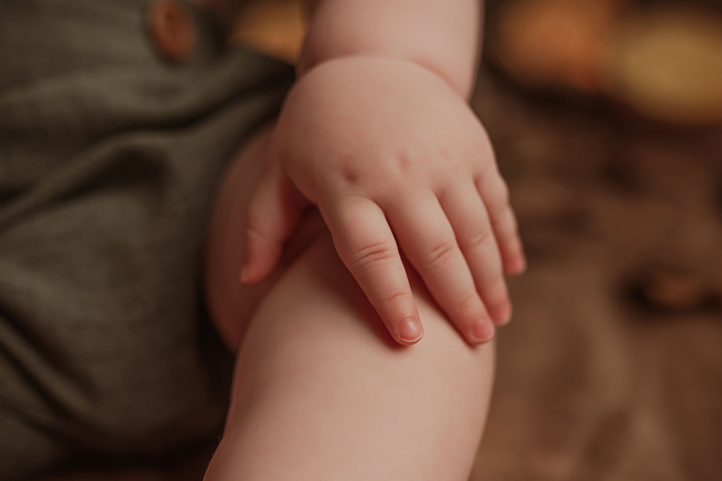 Close-up of a tiny baby hand resting delicately against soft fabric in warm lighting.