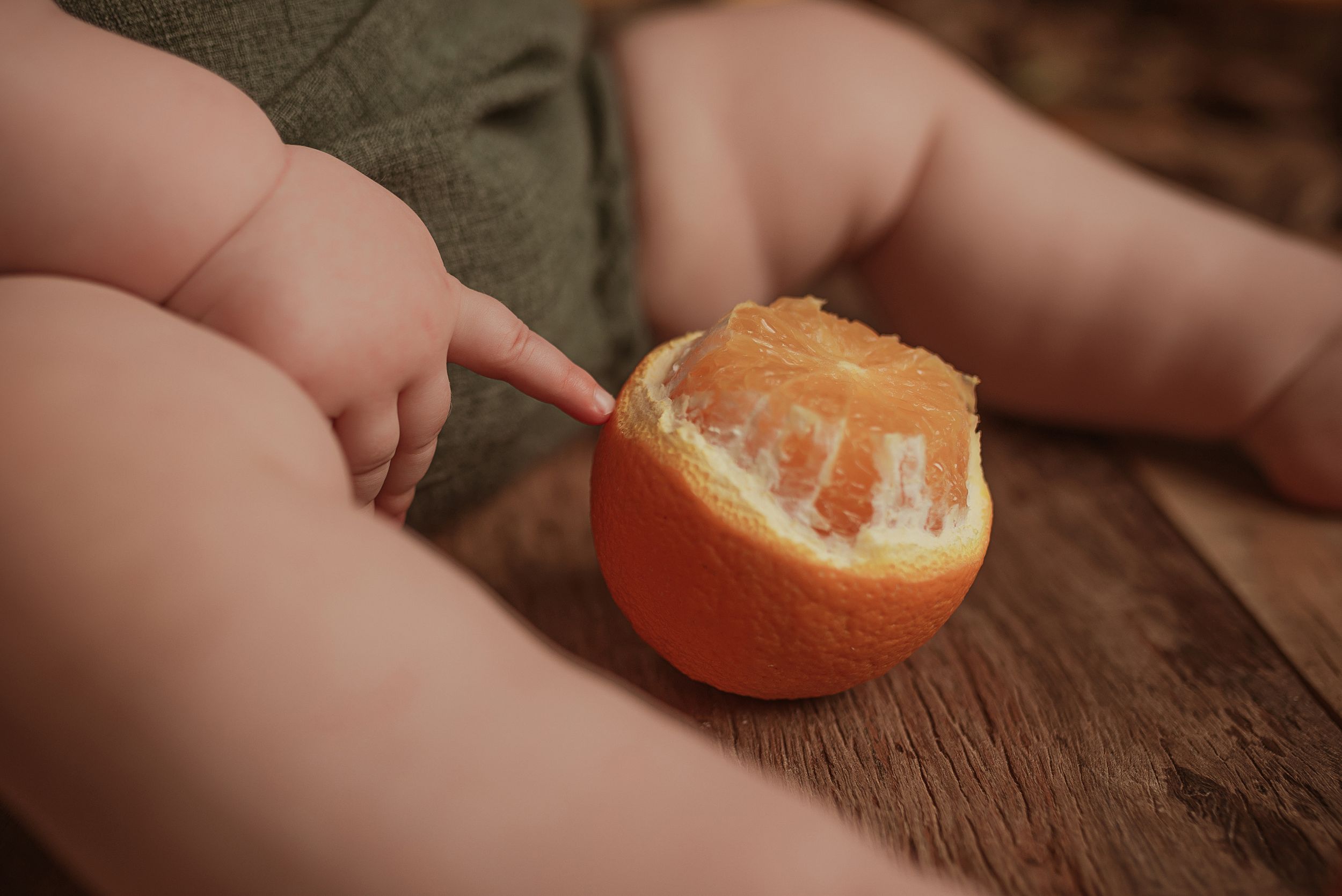 Small hands peel a fresh orange on a wooden surface in warm lighting.