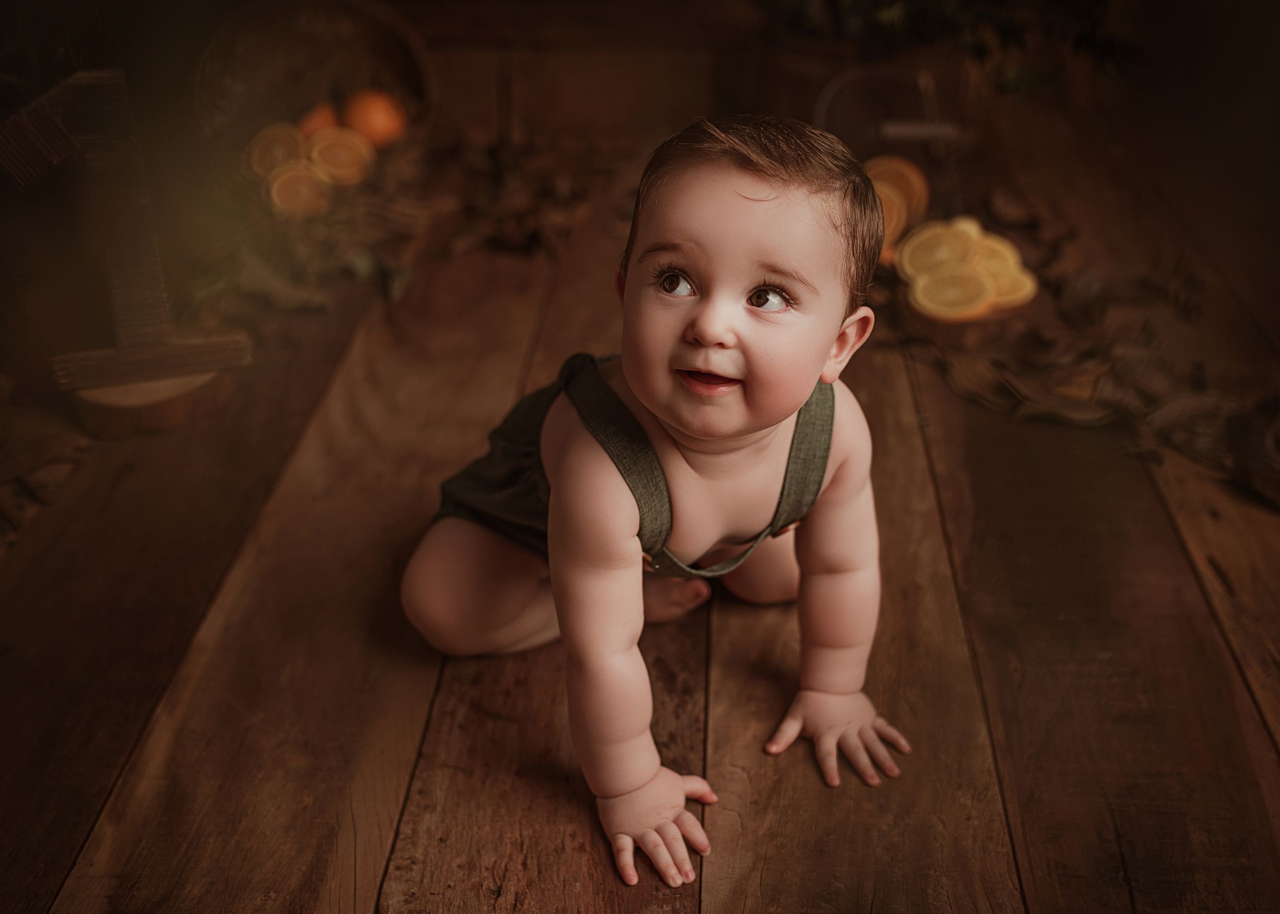 Happy baby crawling on wooden floor with soft brown backdrop in studio portrait setting.