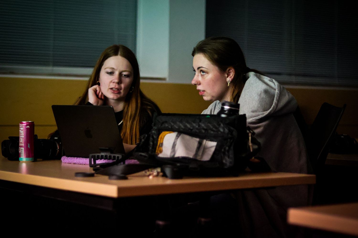 Students working in a dimly lit classroom environment with laptops.