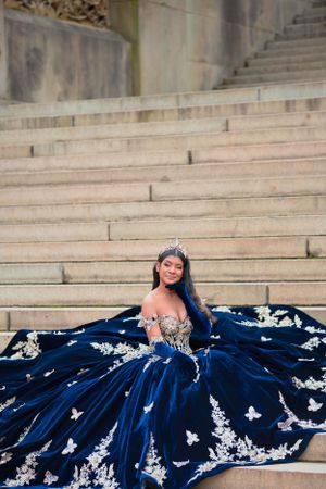 A stunning royal blue ball gown with white butterfly appliques photographed on stone steps.
