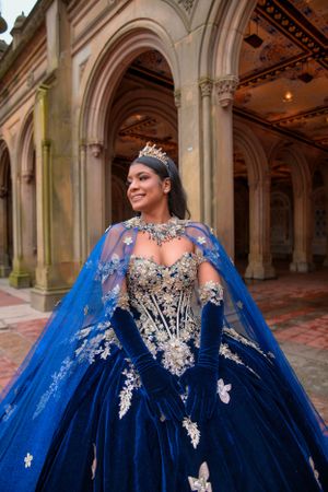 Ornate royal blue ballgown with silver embellishments and butterflies photographed in an elegant arched corridor.