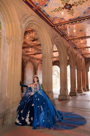 An elegant royal blue gown with intricate detailing stands out against classical stone archways and ornate ceilings.