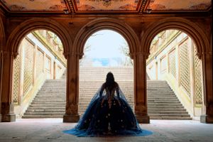 A silhouette sits in an elegant archway between dual staircases at Bethesda Terrace in Central Park, wearing a flowing blue gown.