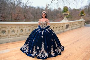 A stunning navy blue and silver quinceañera ball gown photographed on an ornate stone balcony overlooking a lake.
