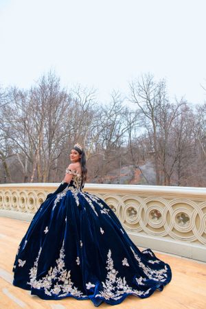 A dramatic navy blue ballgown with white lace appliques photographed on a classic stone balcony during winter.