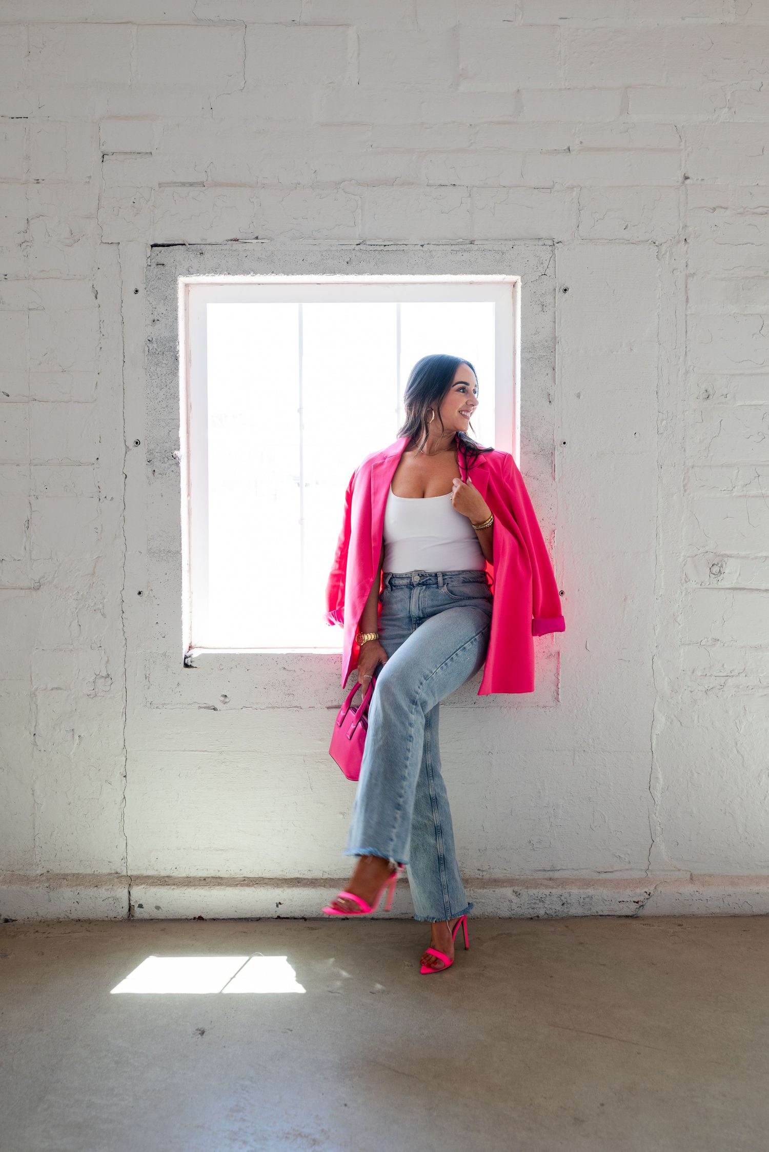 Fashion shot against white wall featuring bright pink blazer, jeans and matching pink accessories.