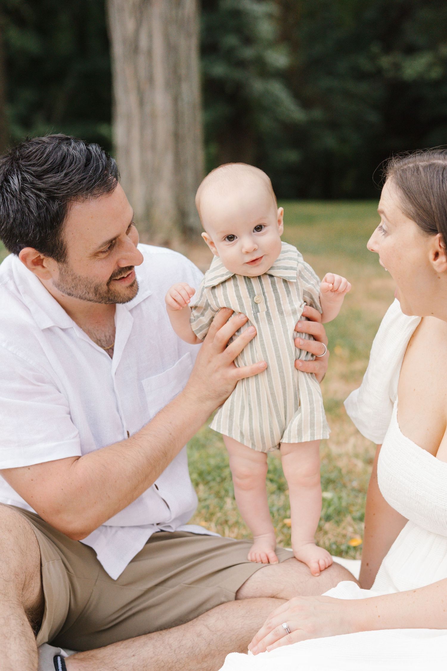 Parents sitting on a white blanket with their toddler standing, creating candid family portraits at Barclay Farmstead.