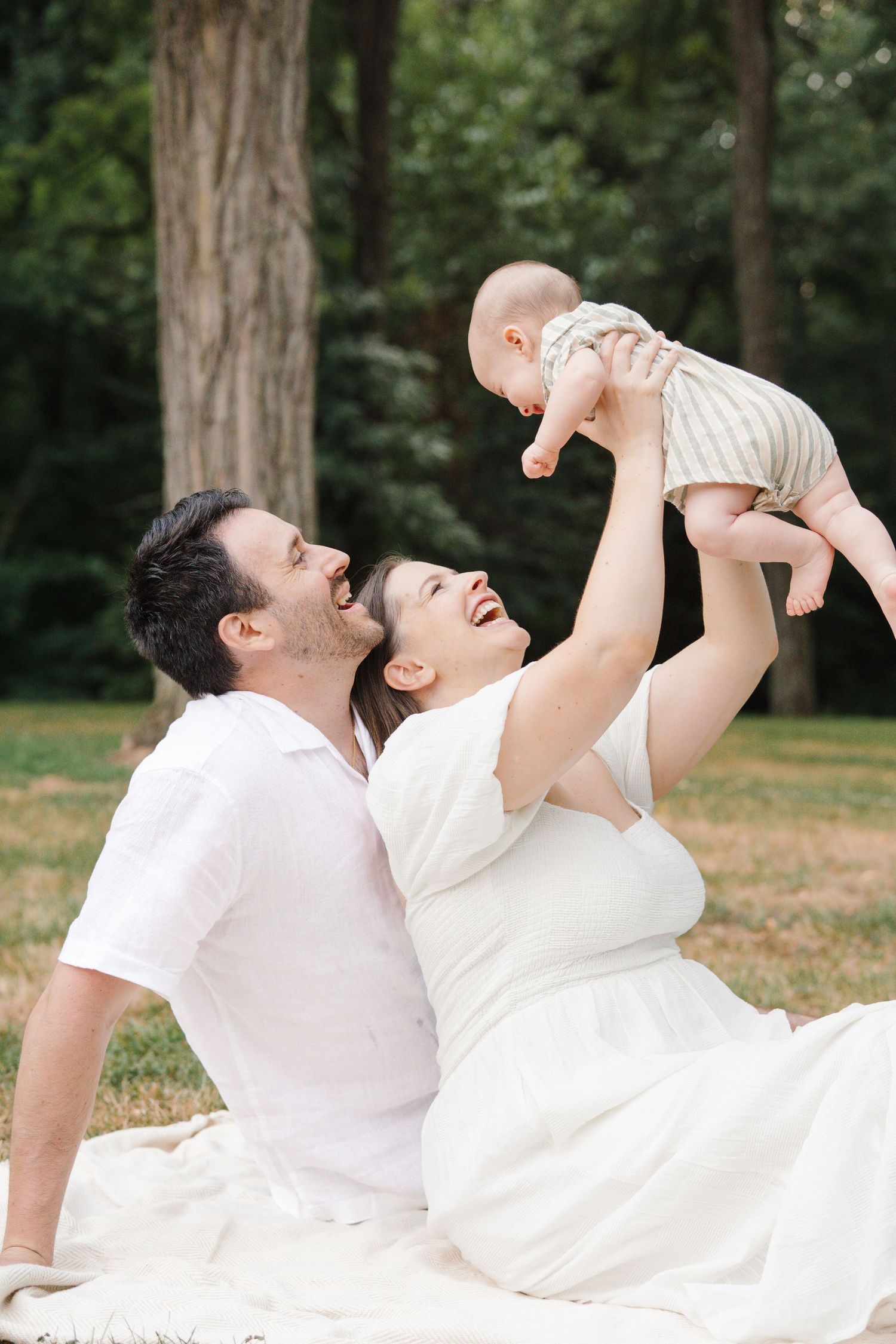 Family enjoying playful moments on a white blanket in the lush green fields at Barclay Farmstead, NJ.