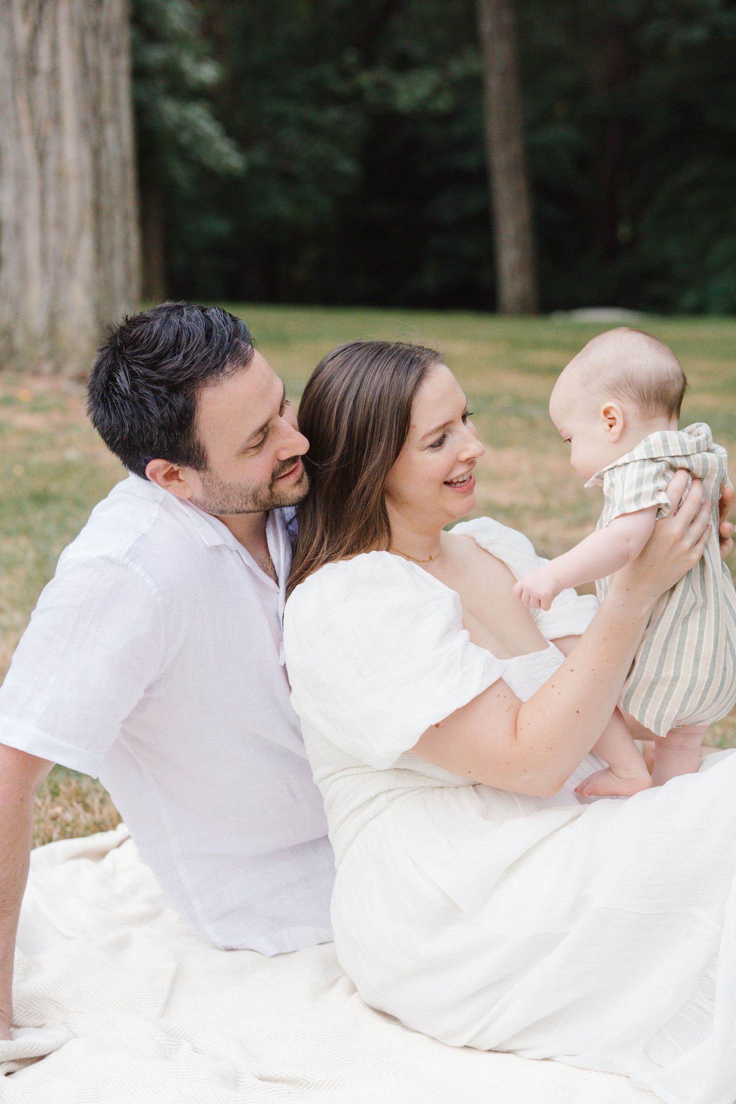 Family of three sitting close on a white blanket, surrounded by nature at Barclay Farmstead in Cherry Hill, New Jersey.