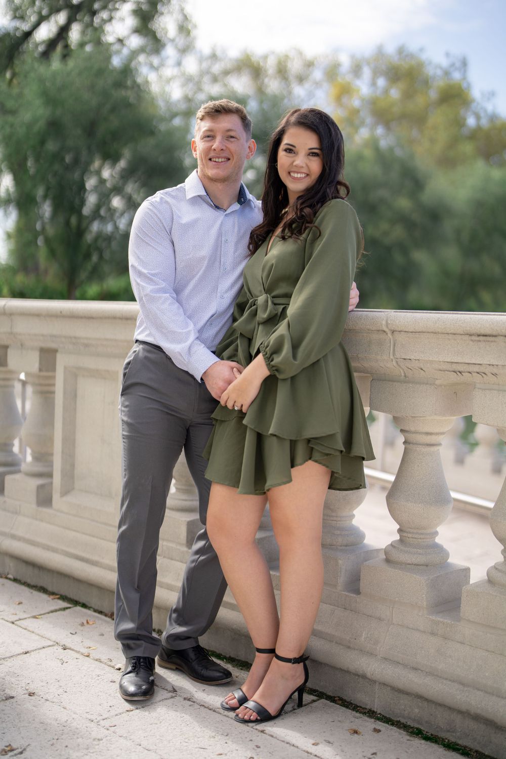 A stylish couple stands close together on an ornate stone balcony during a photo session.