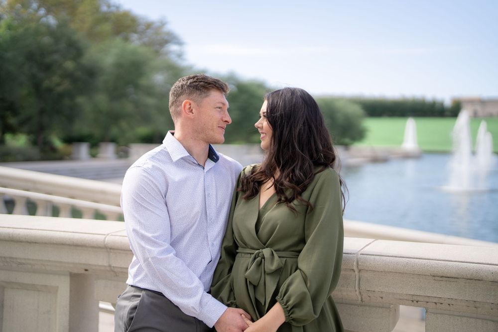 A couple poses by a fountain on a stone balcony during their engagement photo session.