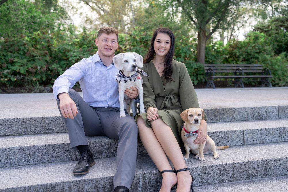 A couple sits on stone steps with their two dogs for an outdoor portrait session.