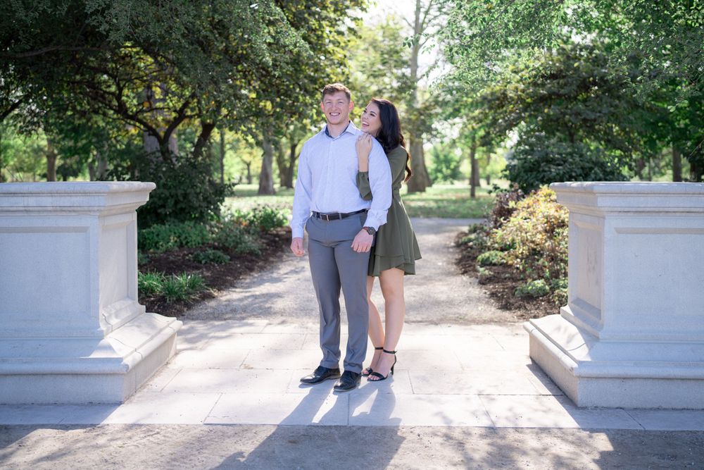 A couple stands between stone pillars on a garden path during their photo session.