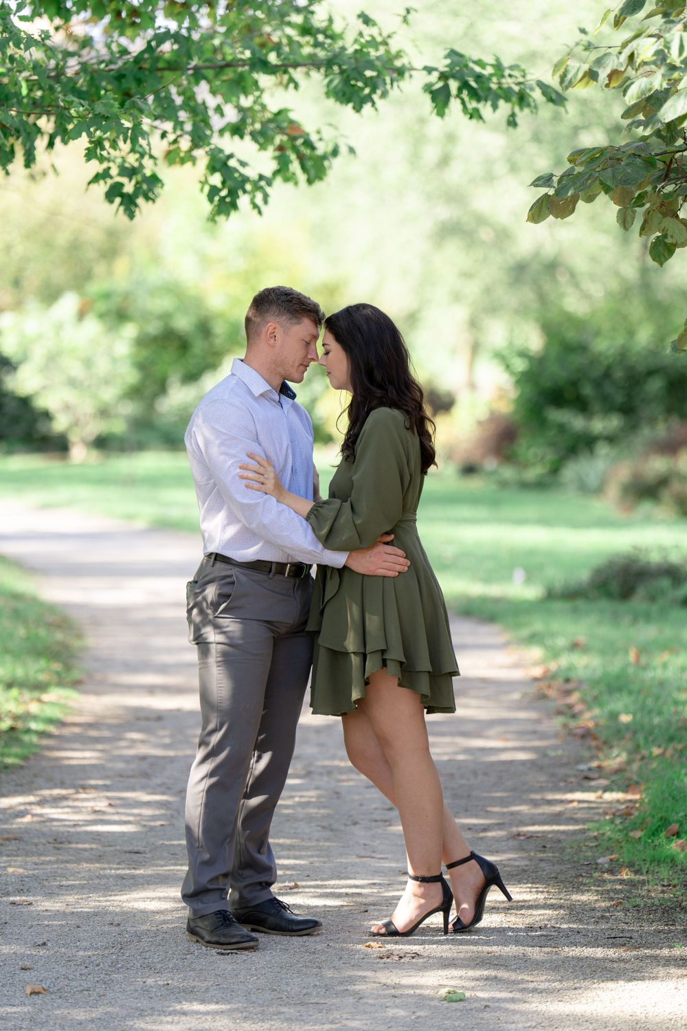 Romantic couple sharing an intimate moment on a tree-lined pathway in a sunlit park setting.