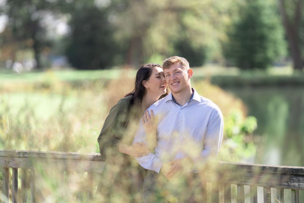 Couple sharing a joyful moment on wooden deck overlooking peaceful pond with natural backdrop.
