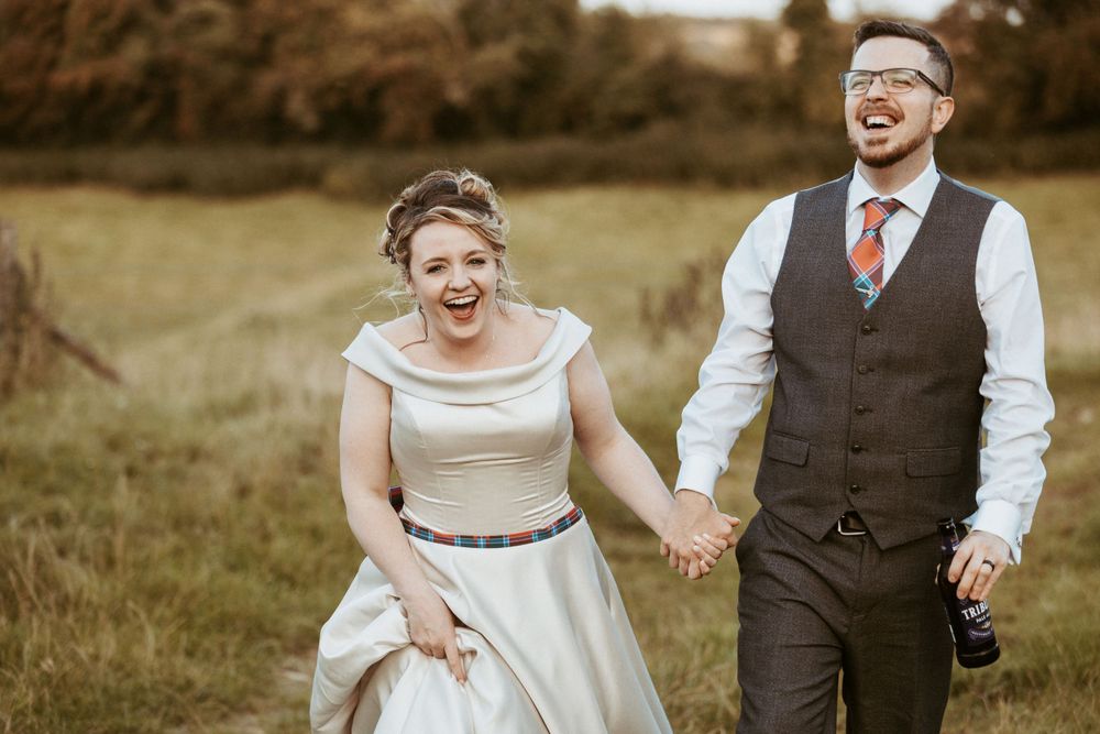 A joyful couple laughs together in a rustic field during their wedding celebration.