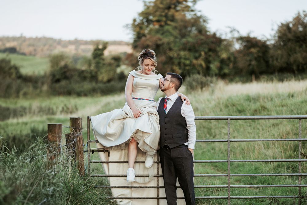 A couple poses playfully on countryside steps with a metal gate in the background.